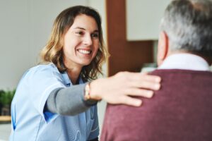 Healthcare provider gently placing a hand on the shoulder of a senior, offering comfort and support before 2-person assist